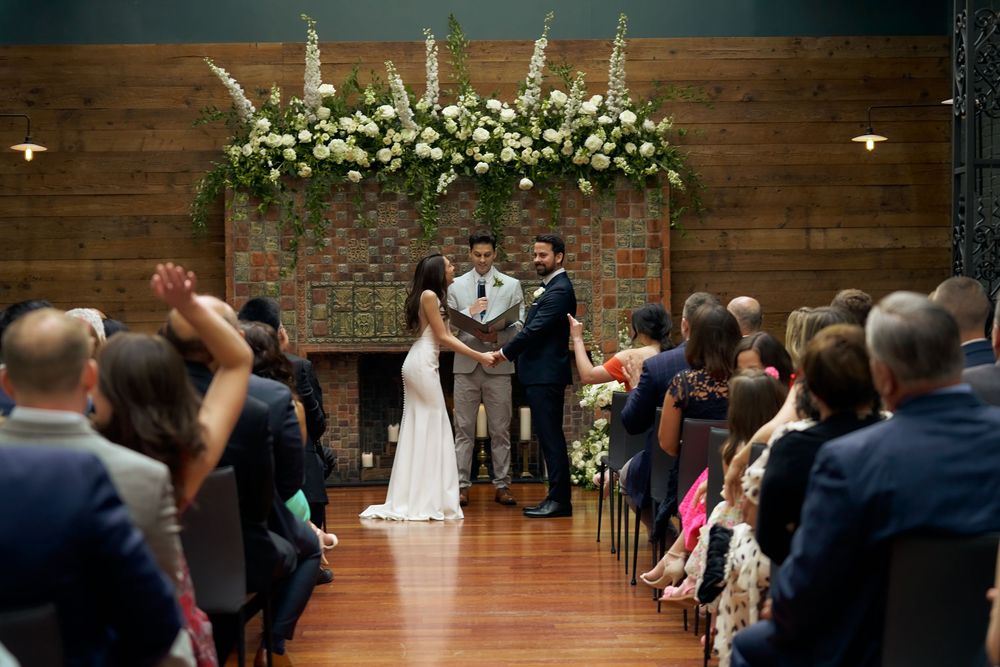 Wedding ceremony guests seated in rows at an elegant indoor venue with decorative floral arrangements at the altar at the Milling Room