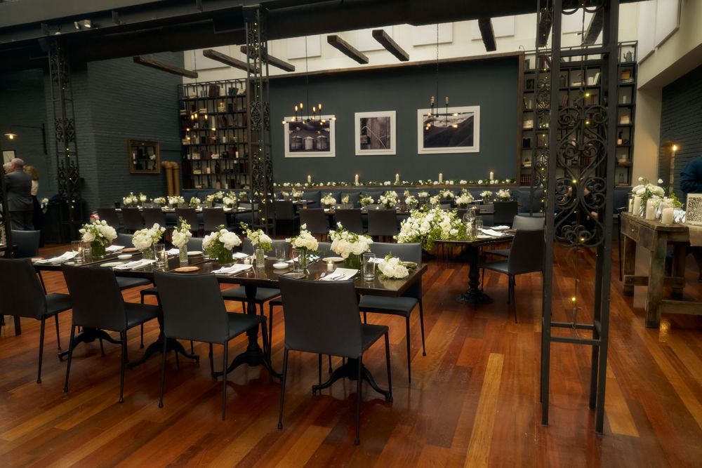 Elegant restaurant dining room with long table settings, dark gray chairs, and framed artwork on charcoal walls at the Milling Room