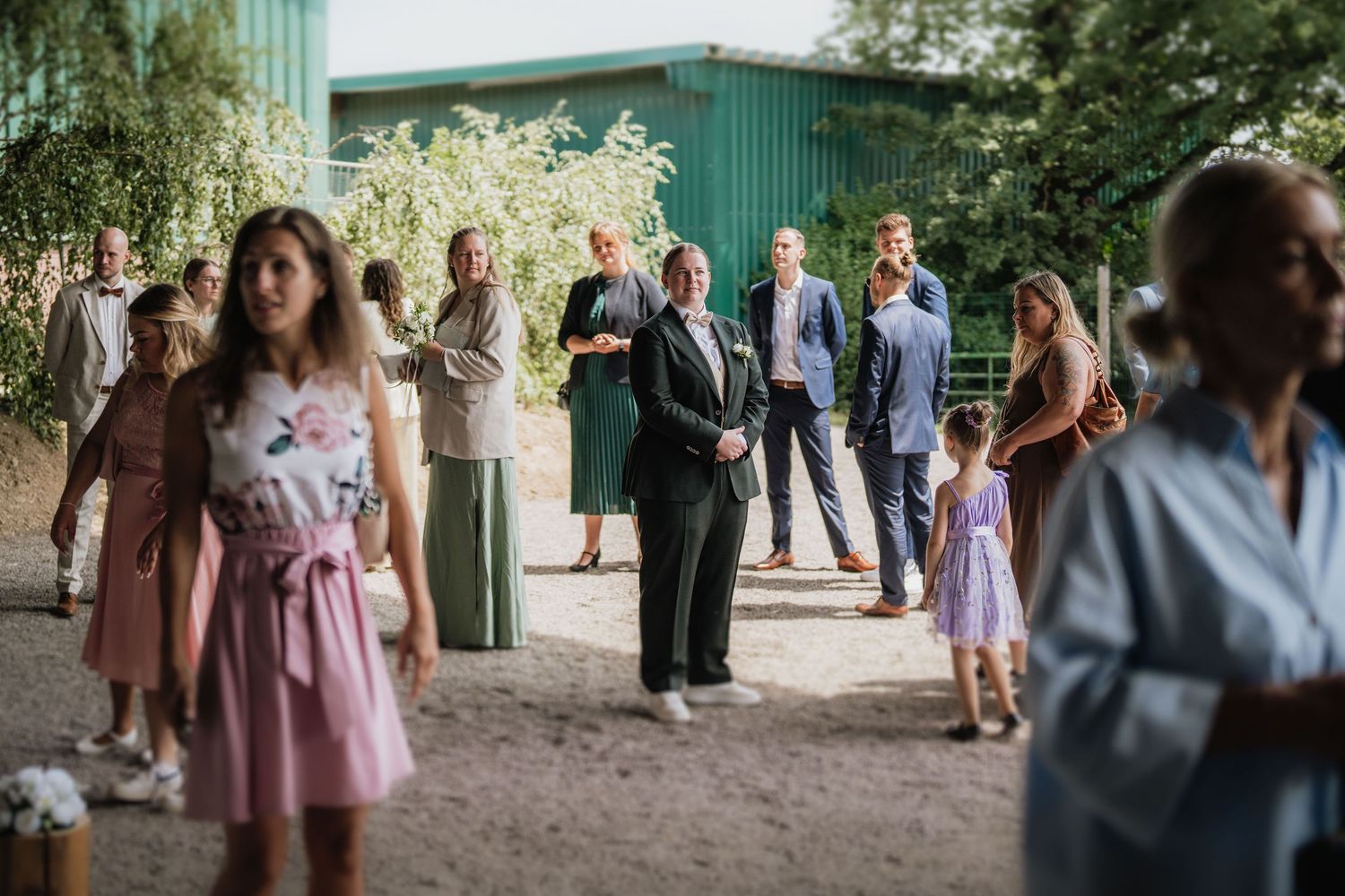Wedding guests in pink dresses gather outside a green building during reception.