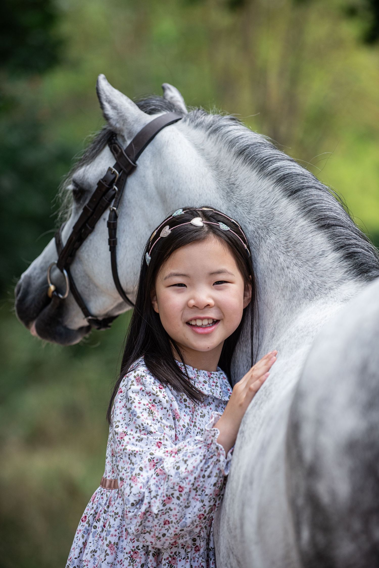 A perfect headshot of show rider Olivia Mu cuddling the neck of her dapple grey welsh show pony Doris, wearing a floral dress