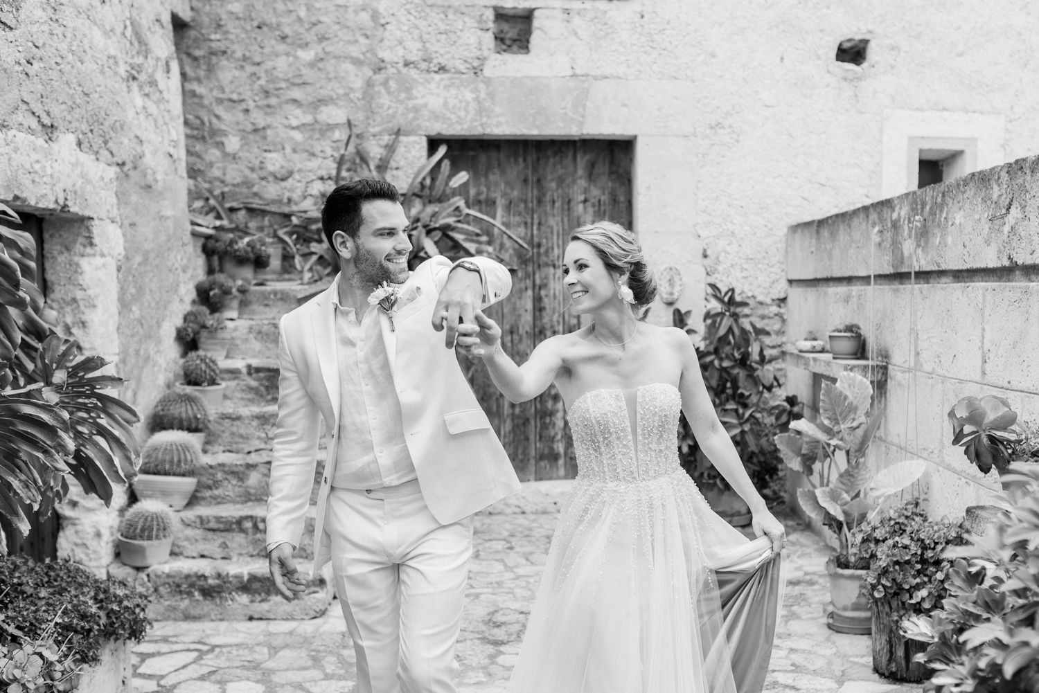 Ein glückliches Hochzeitspaar teilt zärtliche Momente in Schwarz-Weiß-Fotografien vor rustikalen Steinmauern in der Finca Xiclati.
