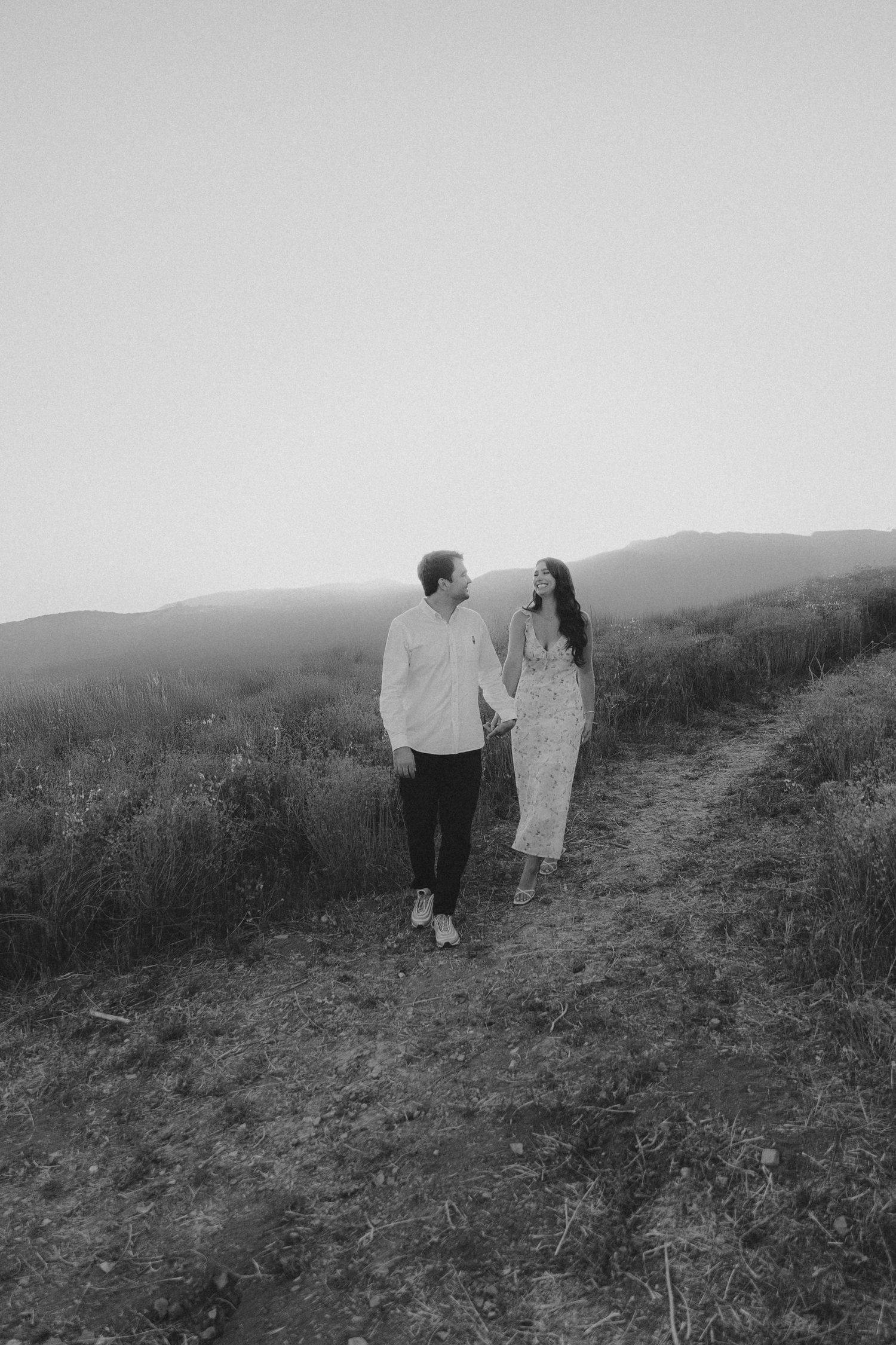 A couple walking together on a hillside trail at sunset in black and white.