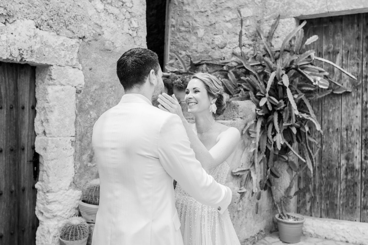 Ein glückliches Hochzeitspaar genießt einen romantischen Moment in Schwarz-Weiß vor einer mallorquinischen, rustikalen Steinmauern.