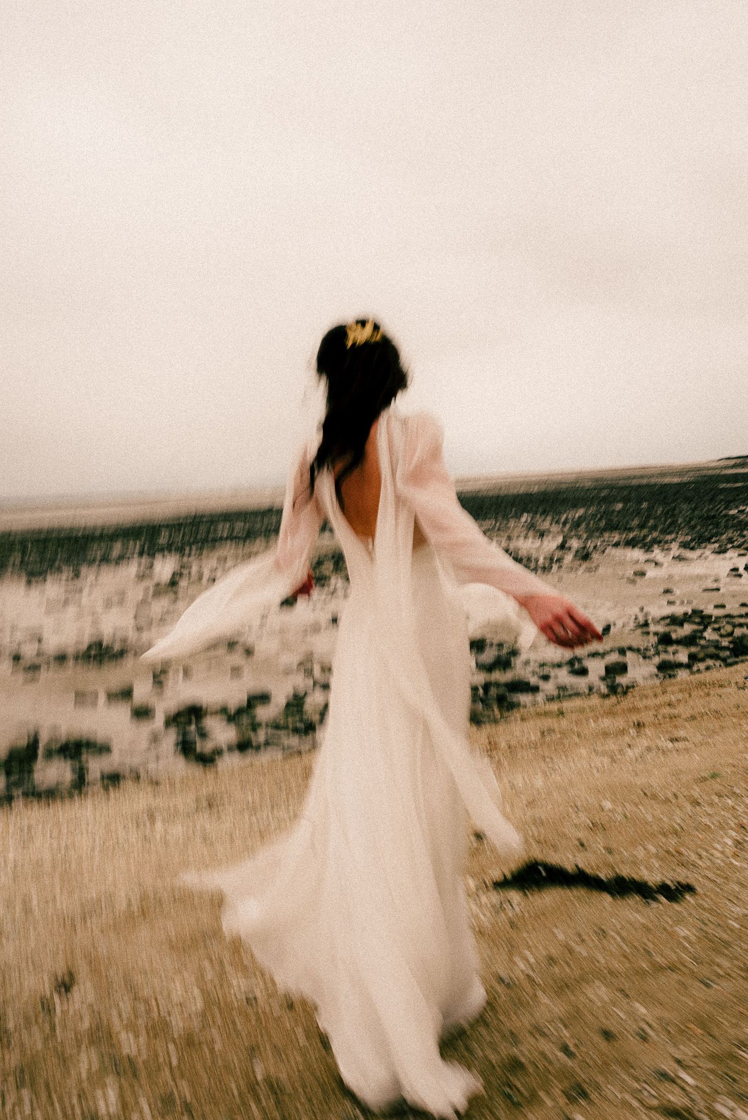 A blurred motion sequence of a person in a flowing white wedding dress spinning and twirling on a beach landscape.