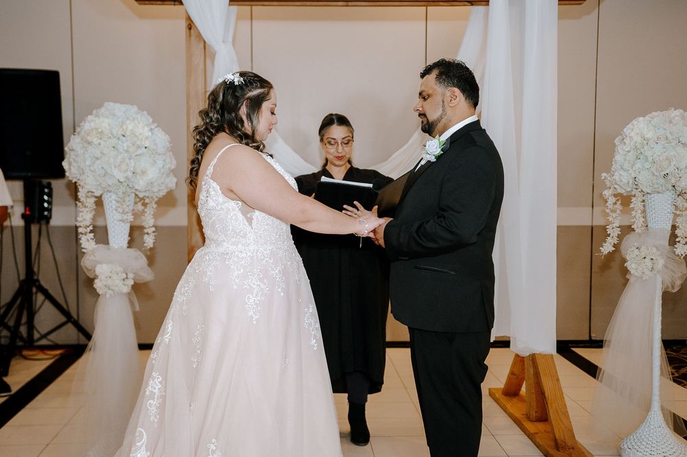 A couple exchanging vows during an intimate indoor wedding ceremony with white floral decorations in the background.