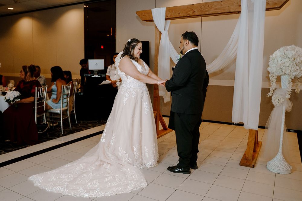 A couple enjoys their first dance at a wedding reception in an elegant venue decorated with white drapes and floral arrangements.