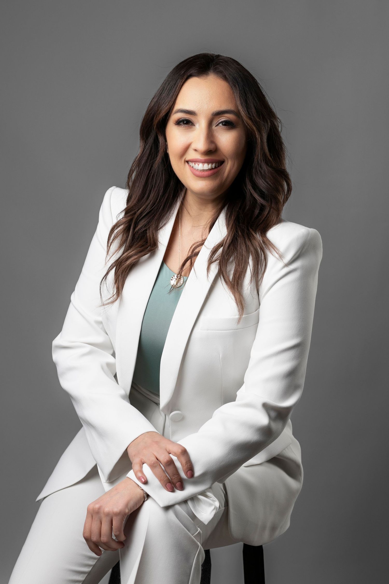 Professional headshot of person in white blazer against gray background.
