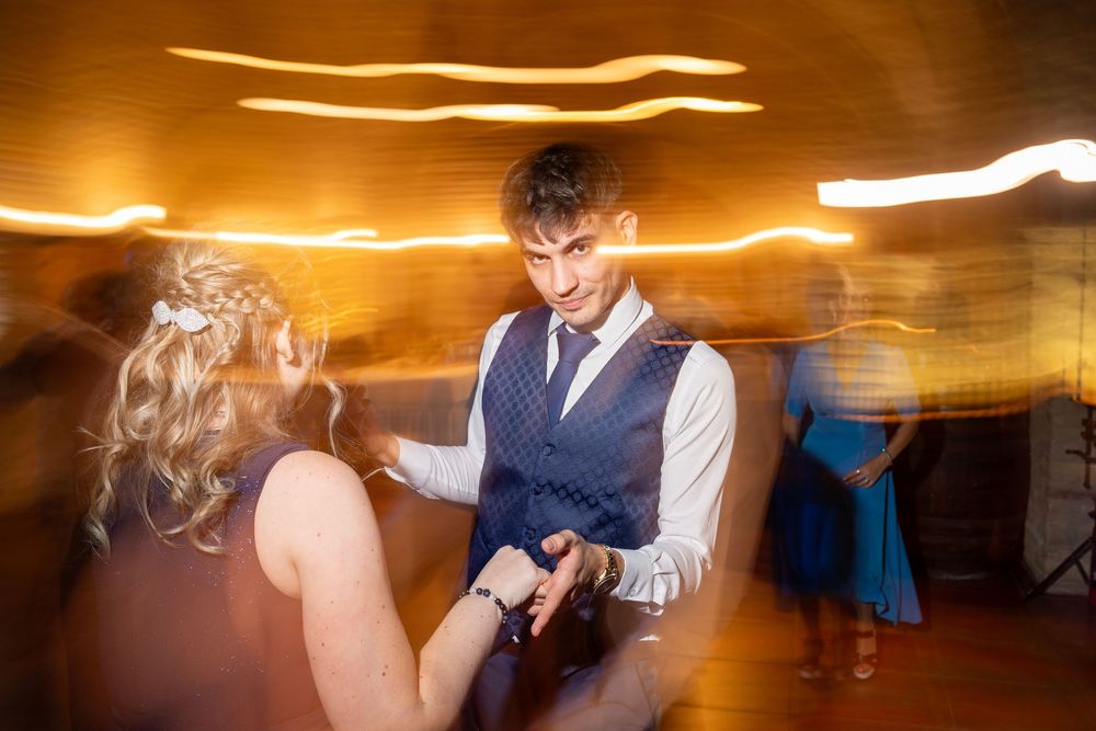 Couple dancing on a wedding reception dance floor with motion blur and warm golden light streaks in the background.