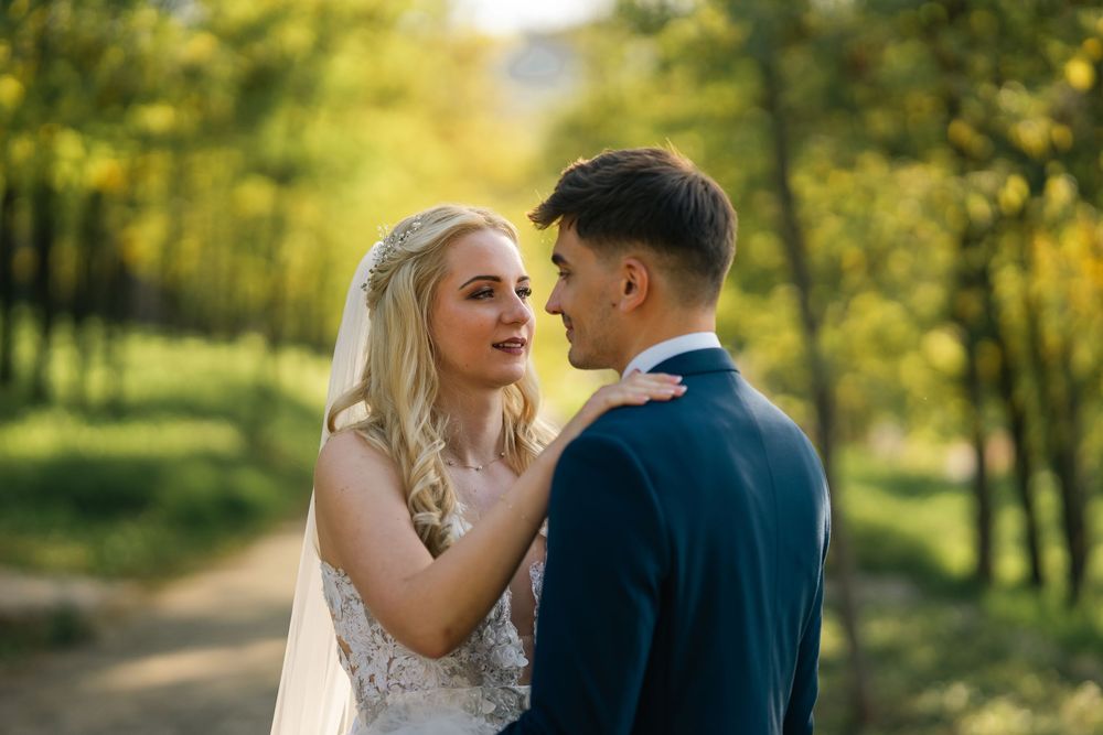 A couple shares an intimate moment on their wedding day along a tree-lined path in warm sunlight.