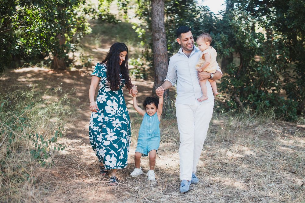 Family walking together on wooded trail during summer photoshoot in matching blue and white outfits.