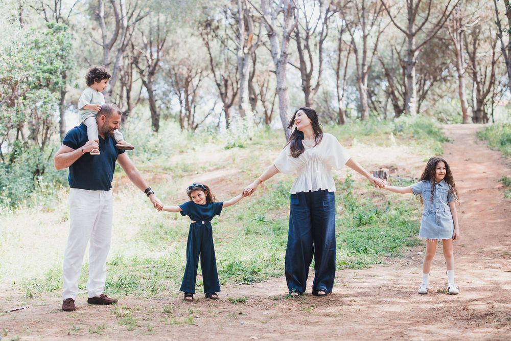 Family group holding hands together while walking on a dirt path surrounded by trees in the forest.