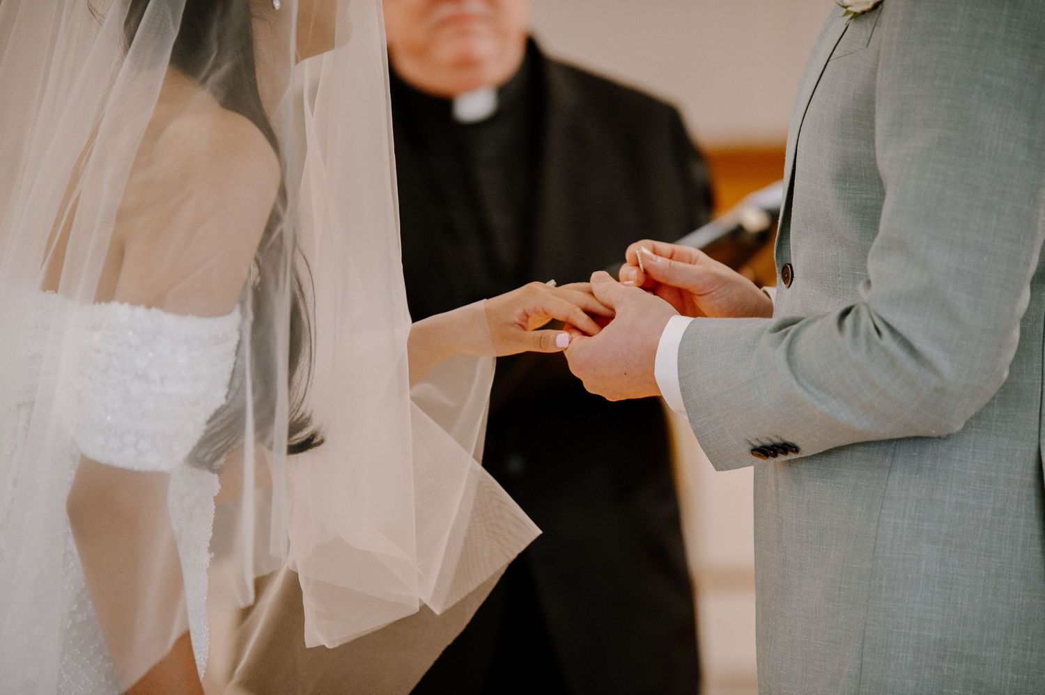 A close-up shot of a bride and groom exchanging rings during their wedding ceremony with an officiant present.