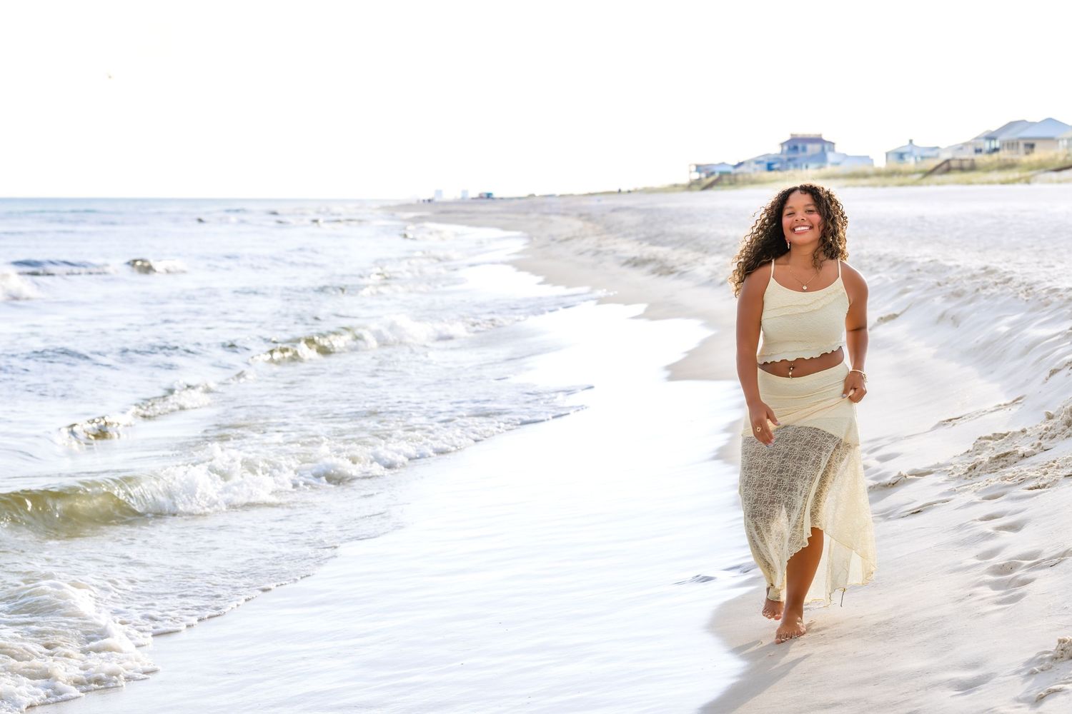 Someone runs joyfully along a sunny beach with waves crashing on the shore in a white sundress.