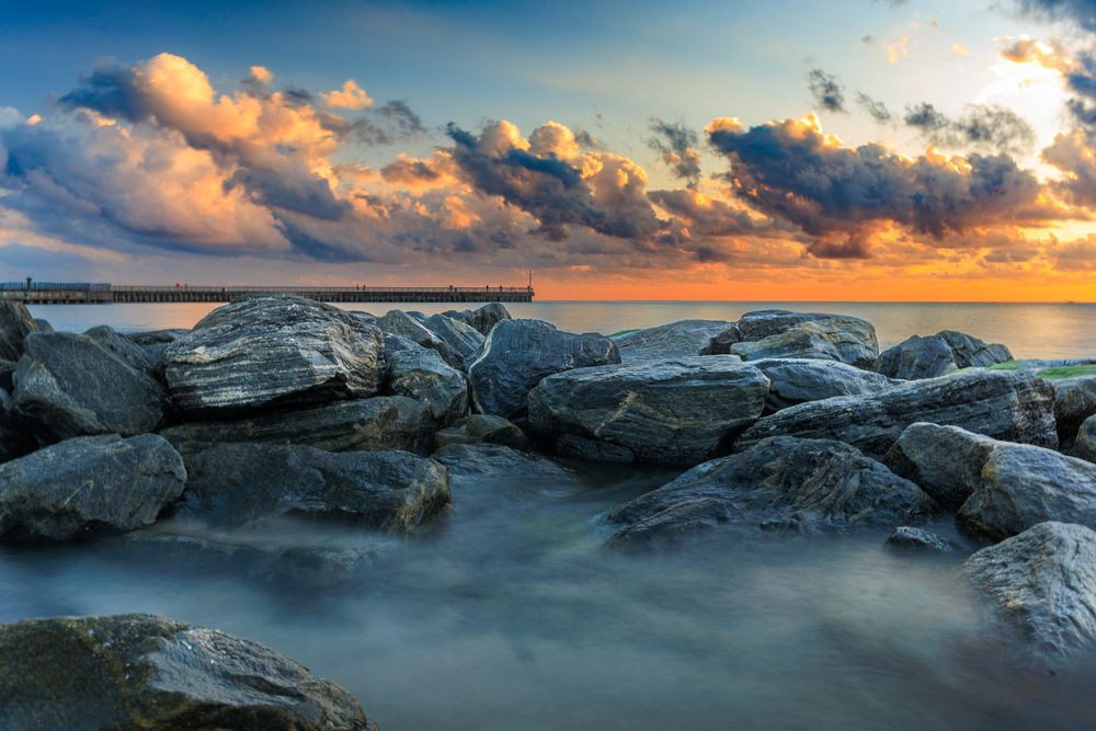 Rocky coastal shoreline with dramatic sky and golden sunlight illuminating the clouds at dusk.
