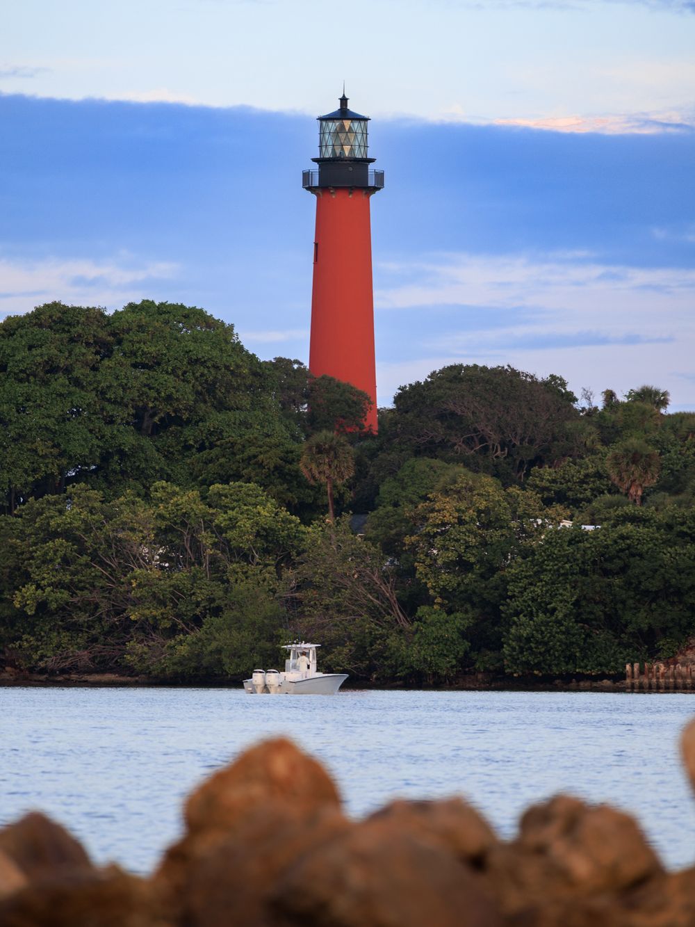 Historic red lighthouse stands tall among trees on shoreline during blue hour.