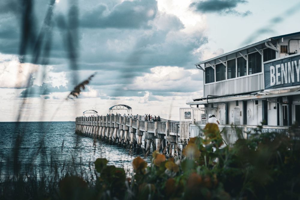 Beachfront restaurant and pier extend into the ocean under moody sky.