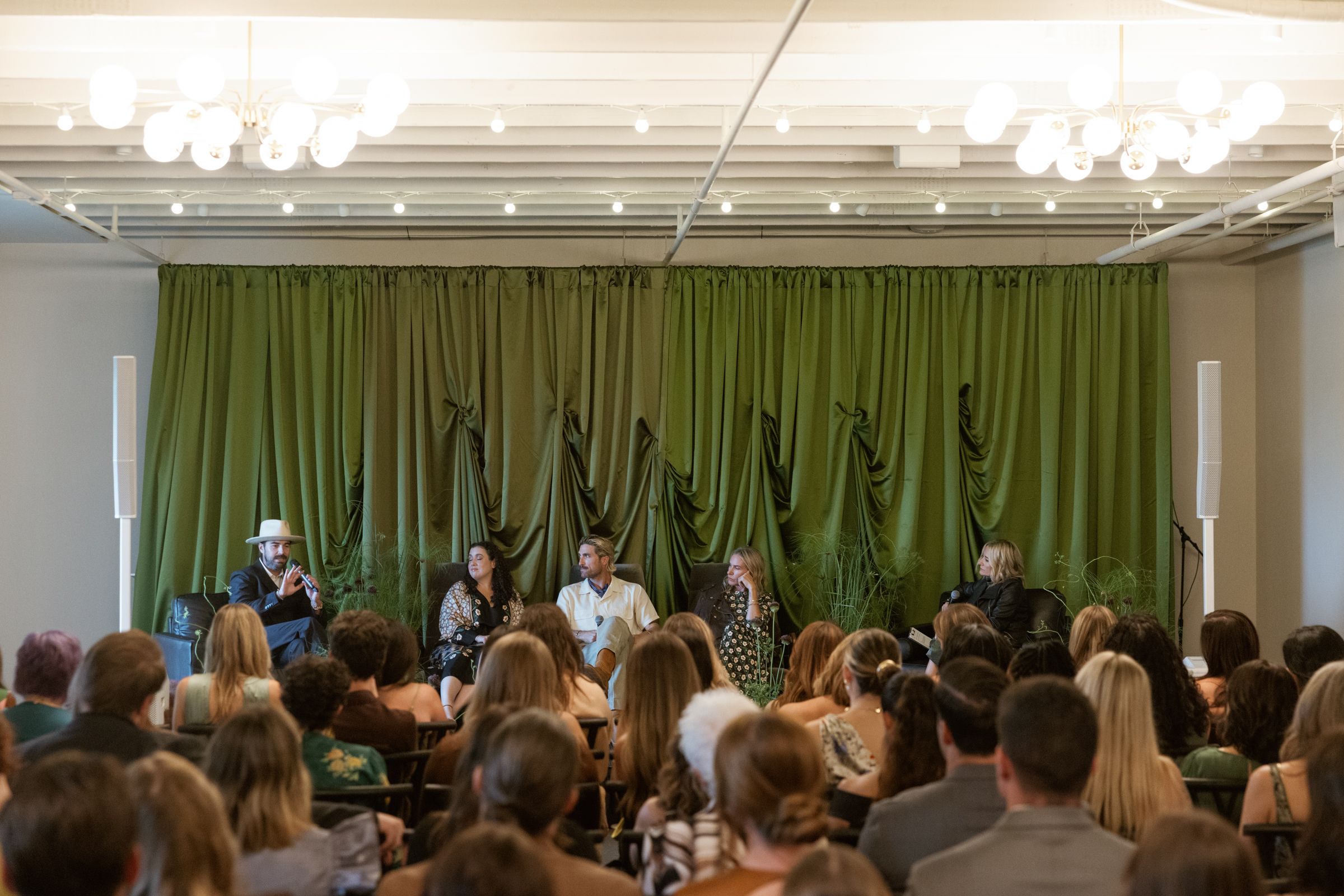A large group of professionals seated in rows at a business conference with green curtains in the background.