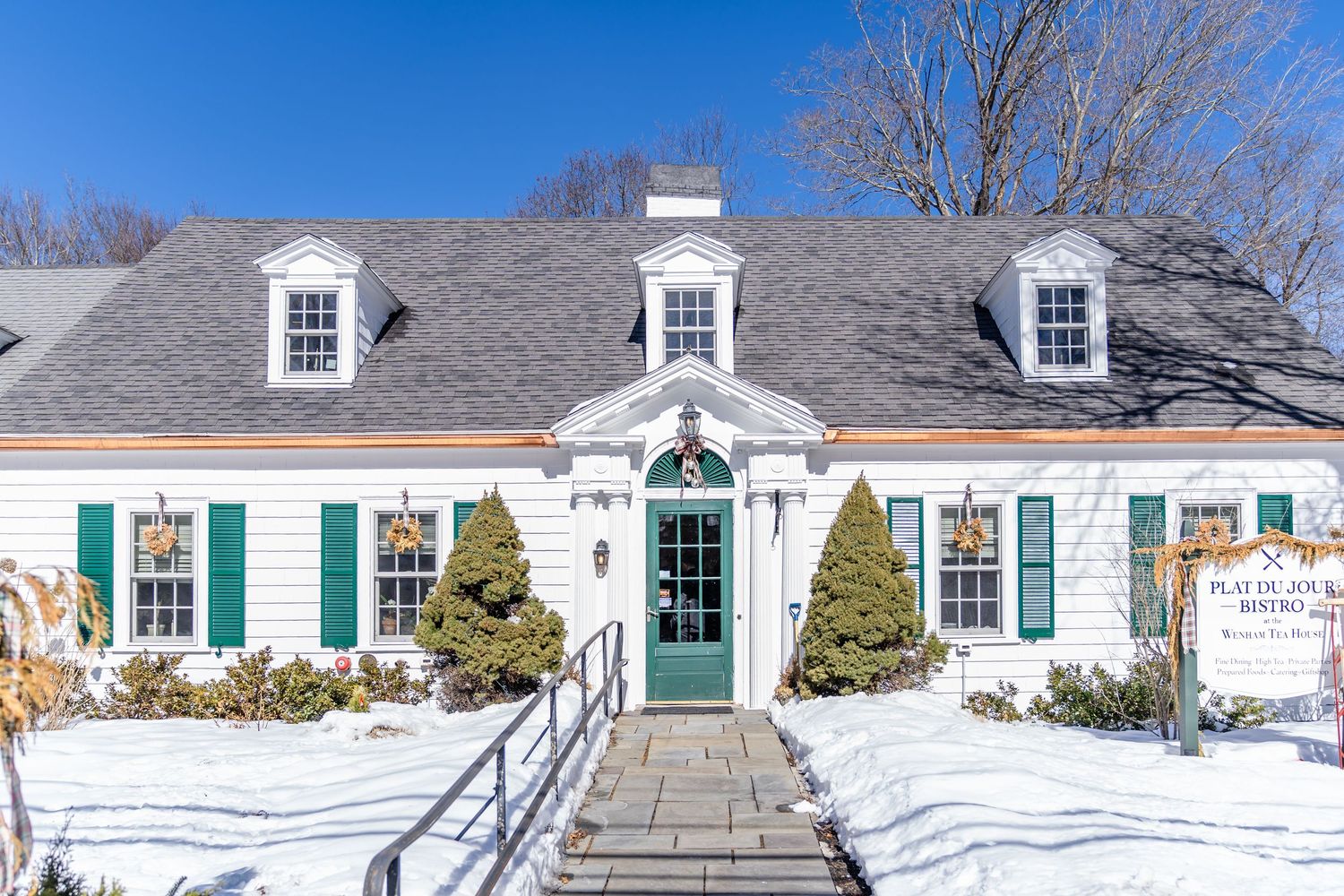 A panoramic view of classic New England style white houses with green shutters arranged along a street in winter.