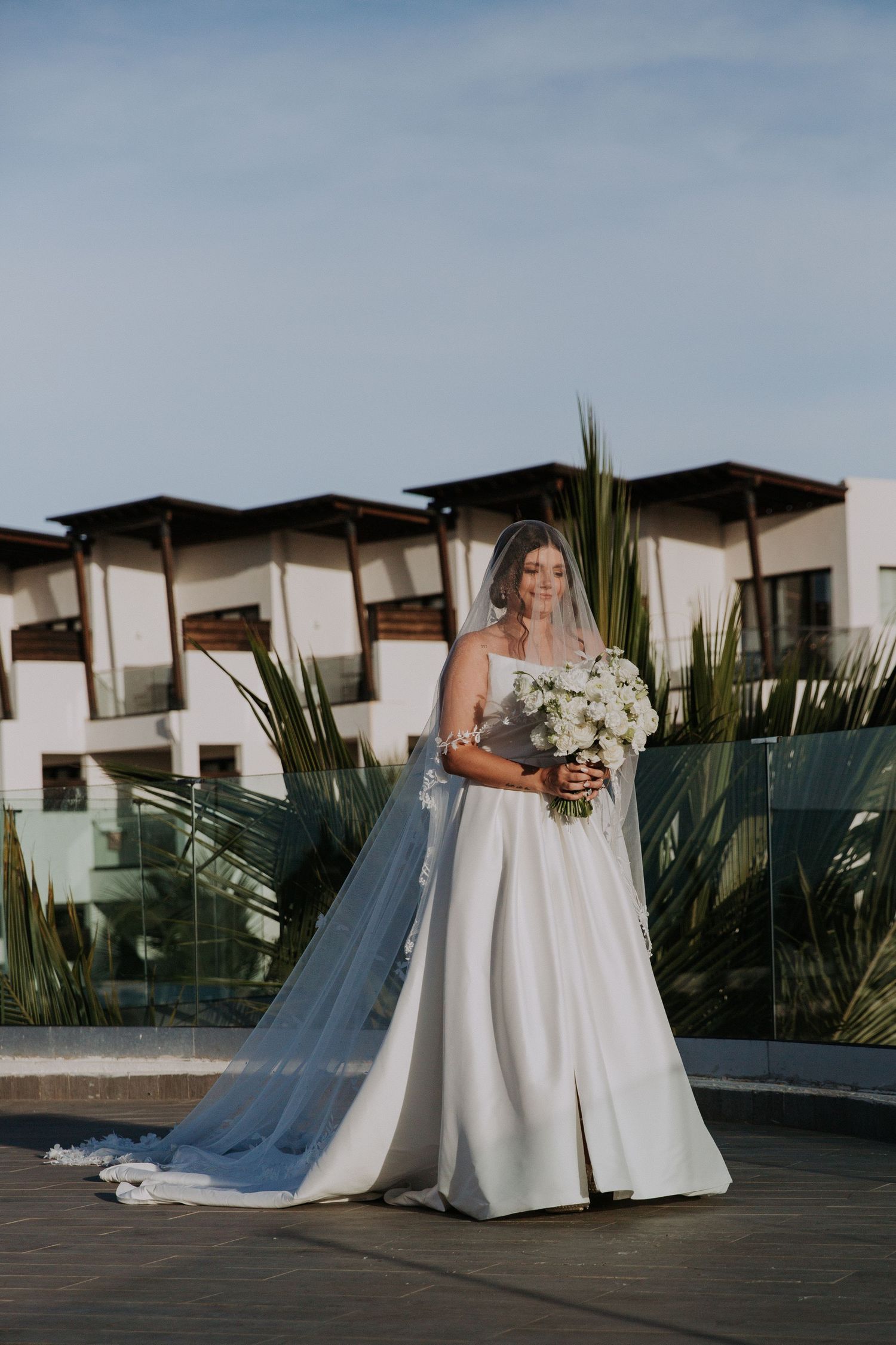 Bridal portrait on rooftop venue showcasing elegant white gown with flowing veil and bouquet.