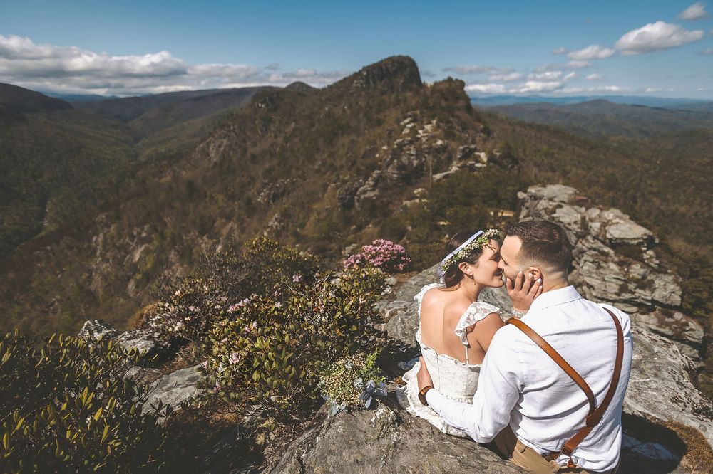A couple embraces on a dramatic mountain overlook under blue skies.