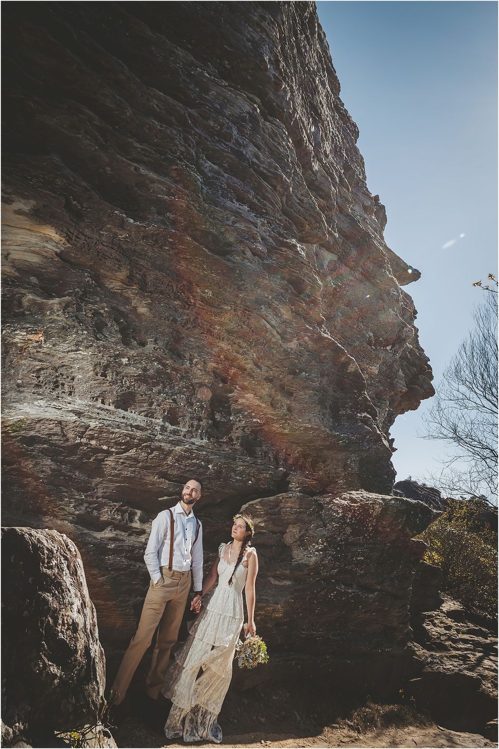 A romantic wedding portrait against towering sandstone cliffs and blue sky.