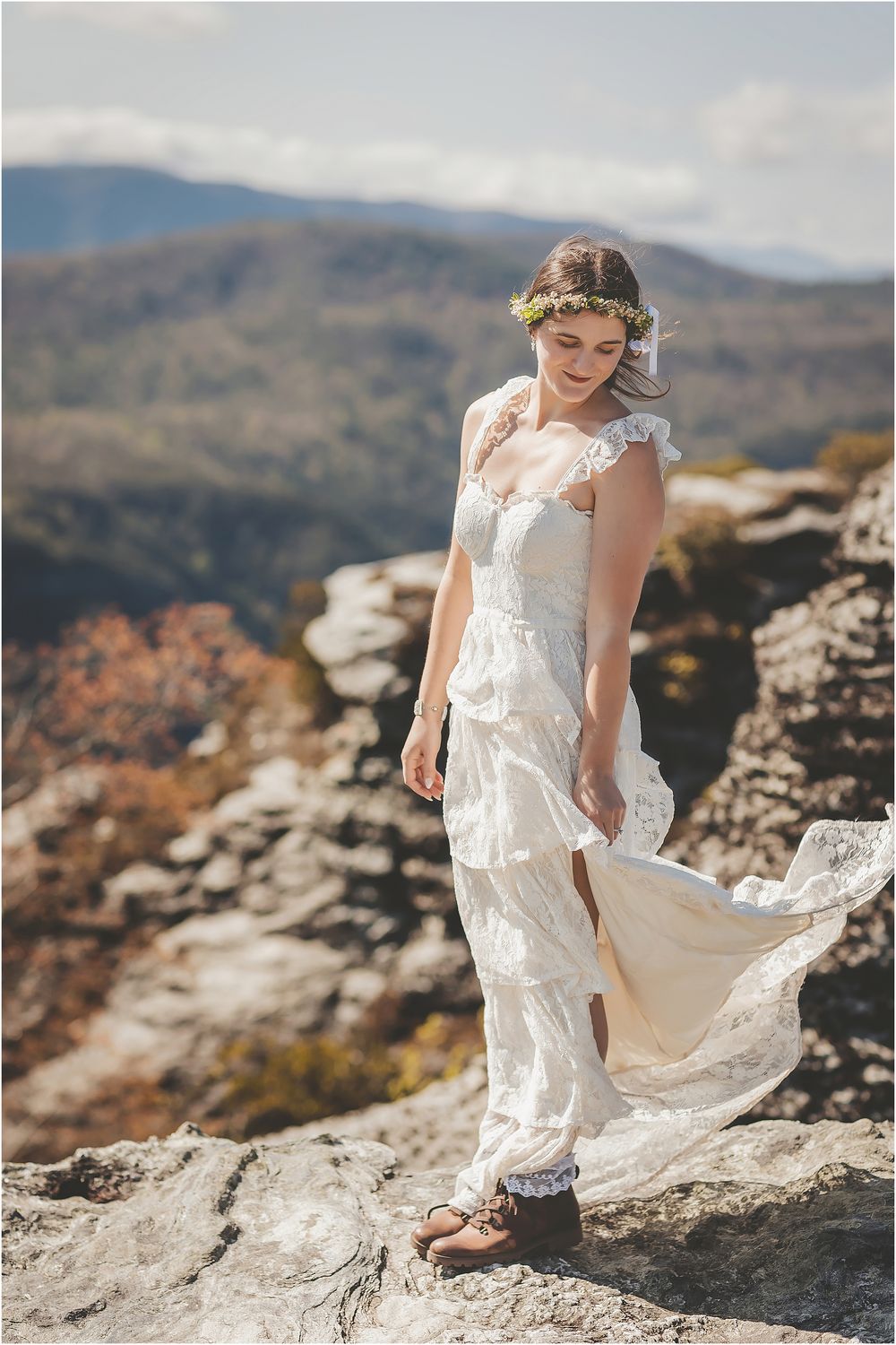 White wedding dress flowing in the wind on a mountaintop with rolling hills in background.