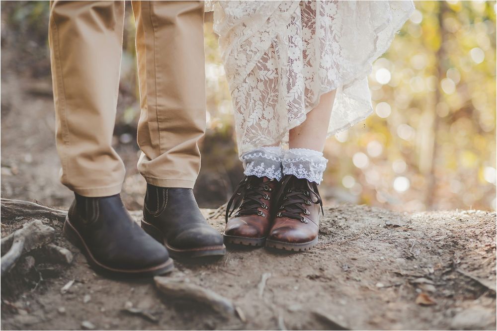 Close-up of boots and lace dress hem standing on rocky ground during an outdoor wedding.
