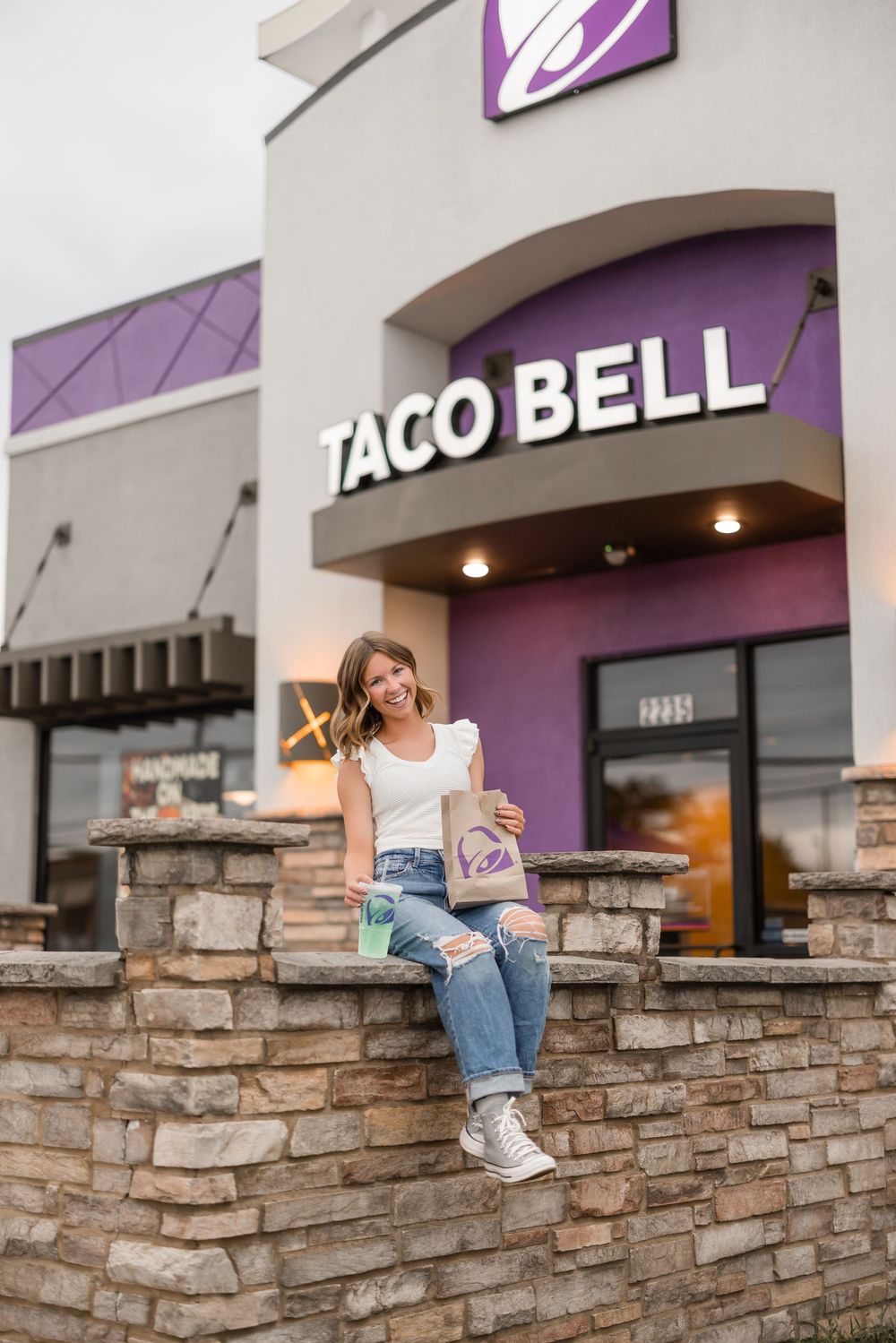 Stone wall outside Taco Bell restaurant with customer seated casually on the ledge.