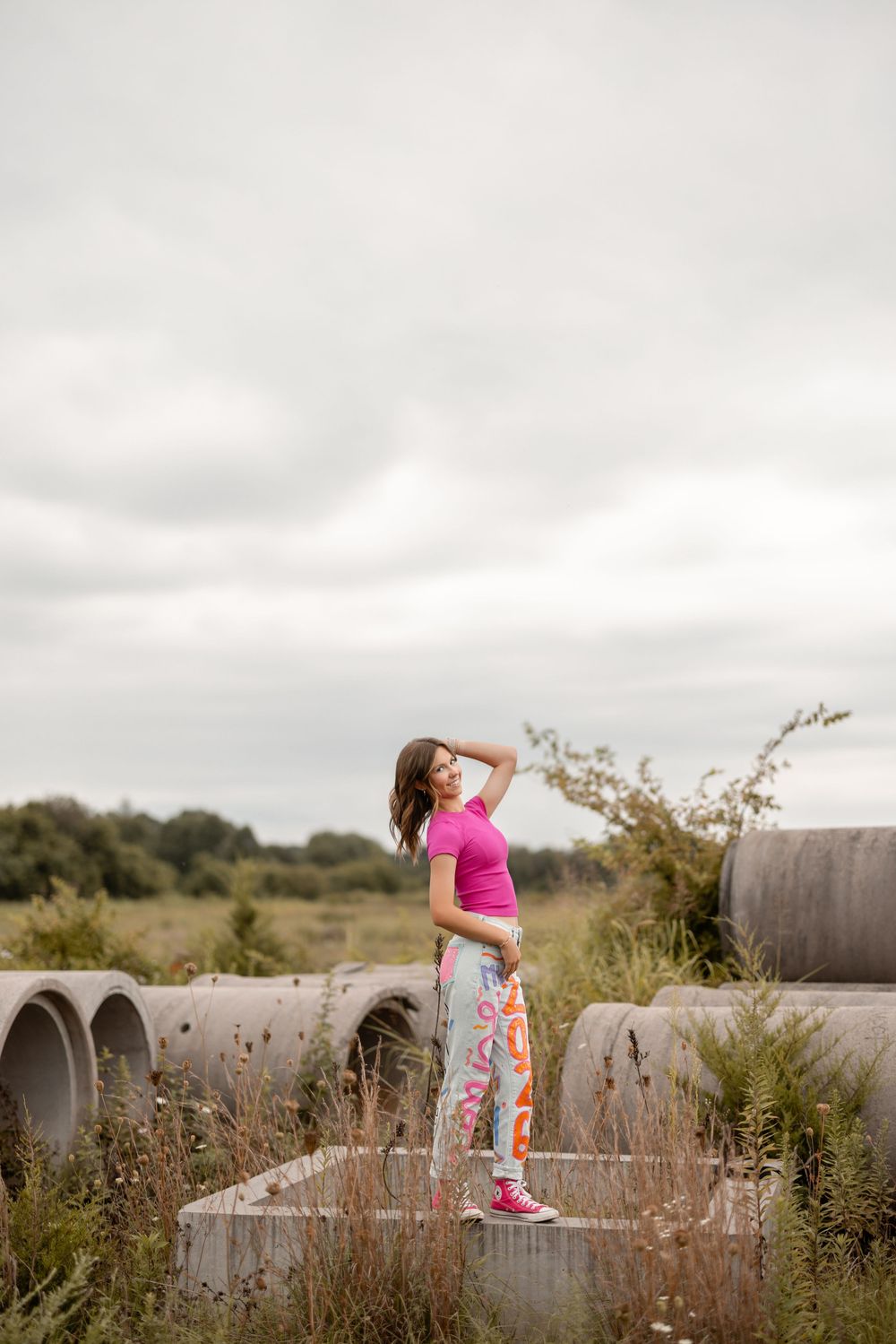 A sequence of four shots shows someone in pink performing energetic poses on concrete drainage pipes in a rural field.