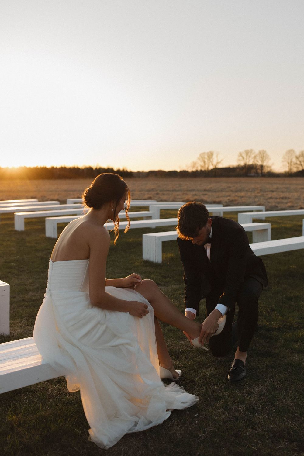 A couple sitting on white benches in a field during golden hour at their wedding.