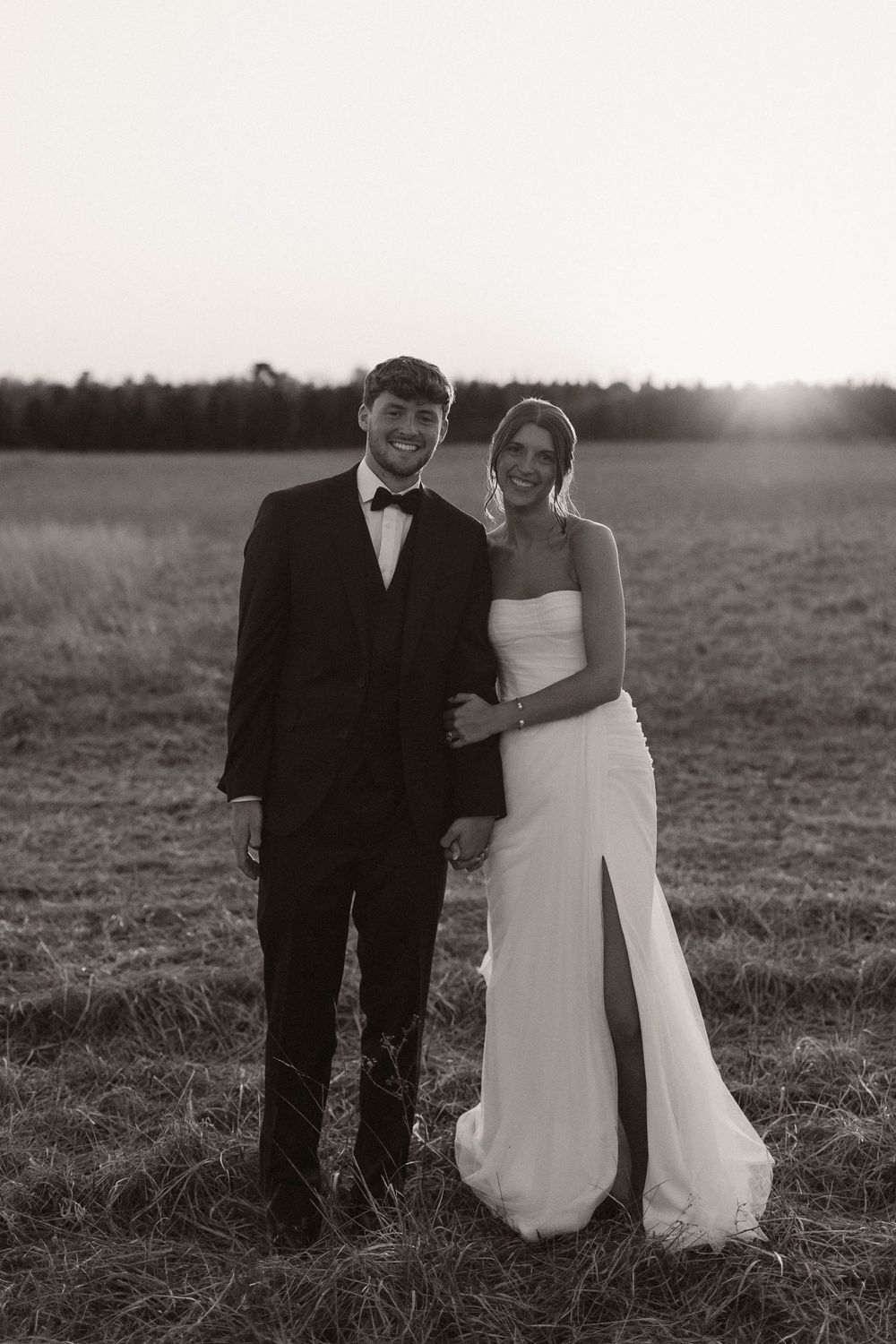 A romantic black and white portrait of newlyweds in formal attire standing in a field.