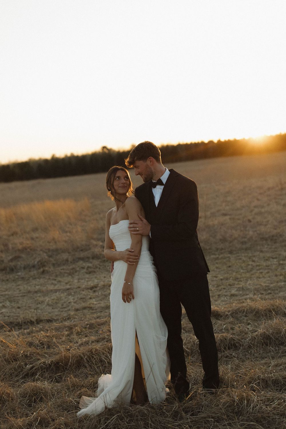 Newlyweds embrace in a golden sunset field during their wedding photoshoot.