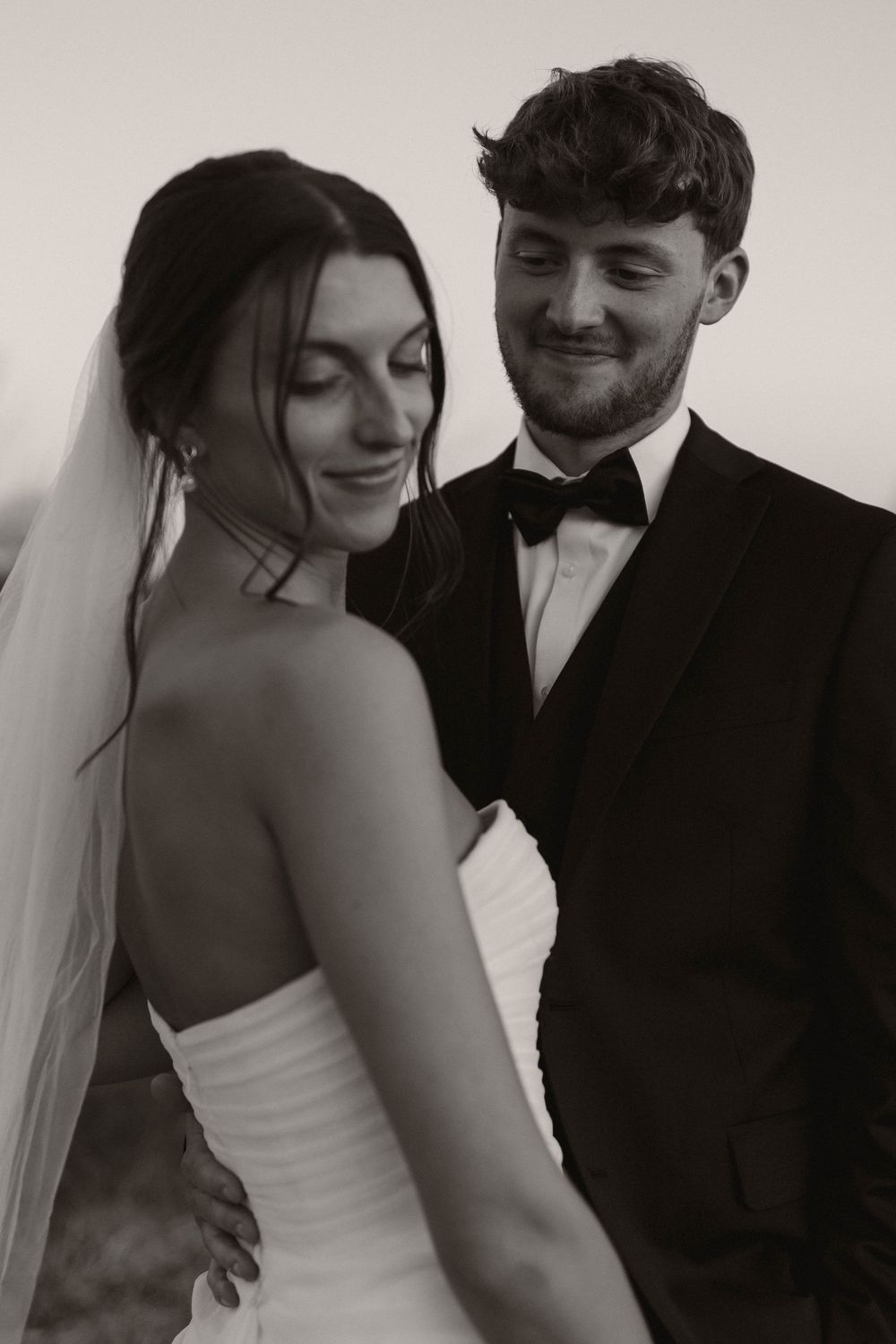 Black and white portrait of newlyweds sharing intimate moment in formal attire.