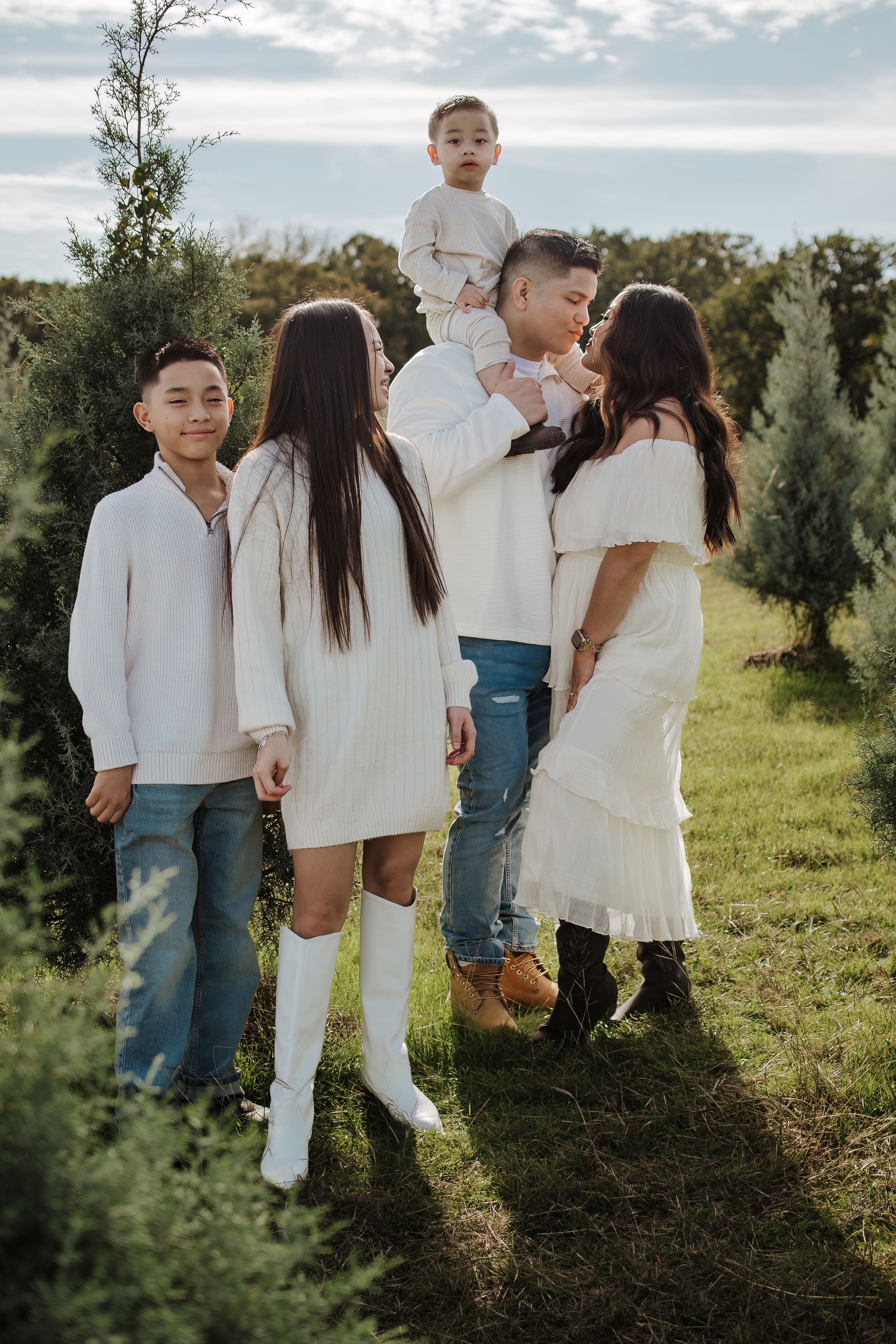 Dfw Tree Farm Family wearing coordinated white outfits posed together in a grassy outdoor setting.