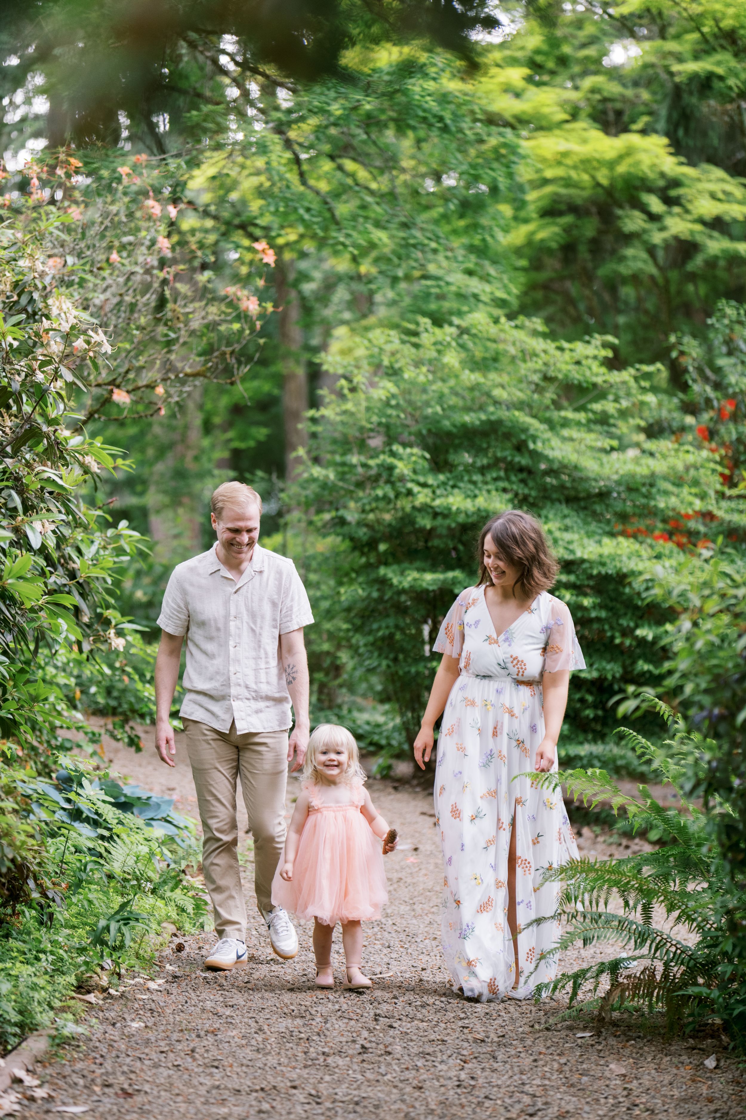 A family walks together on a peaceful forest path surrounded by lush green trees and foliage.