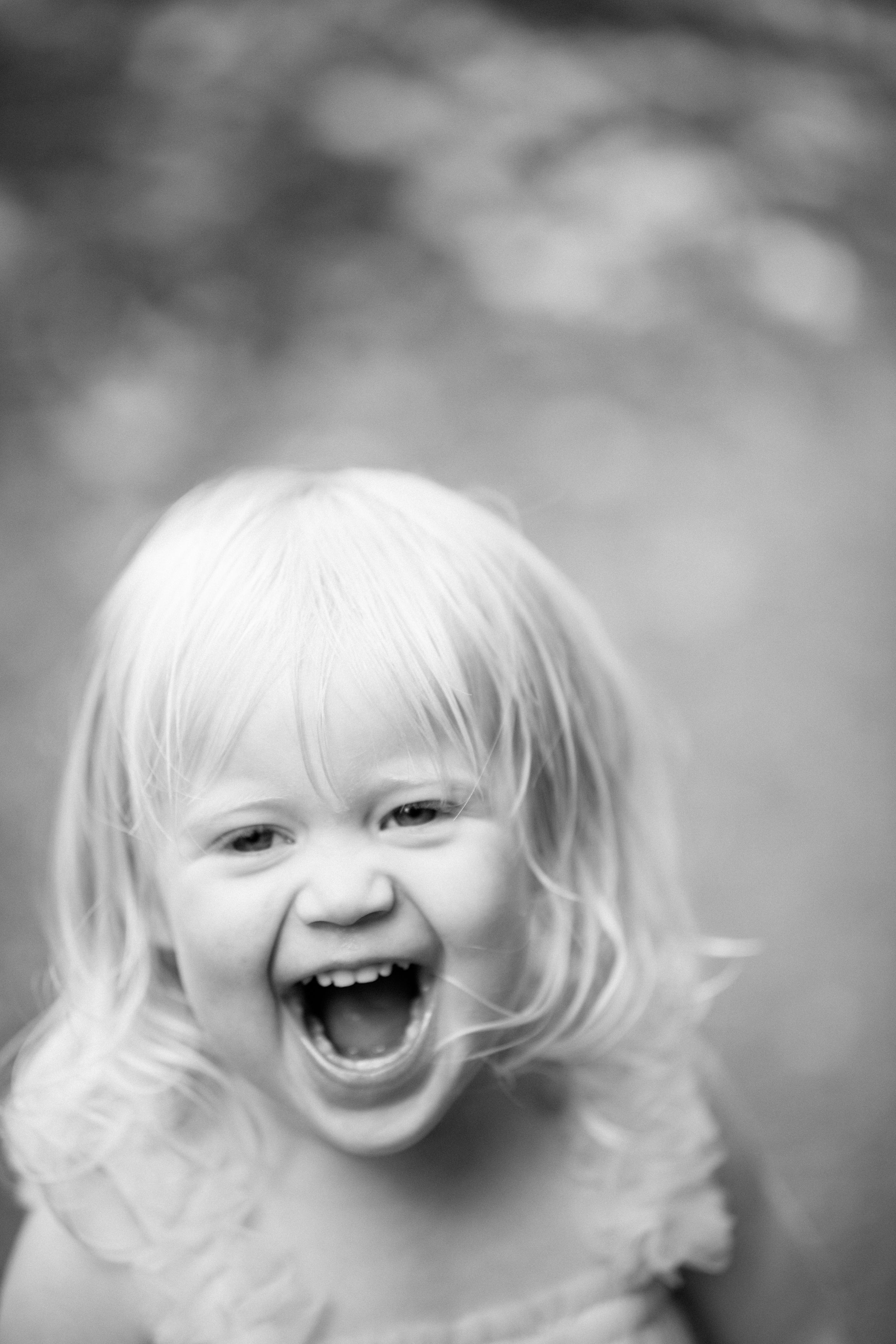 A black and white portrait capturing pure joy and laughter with bright light-colored hair.
