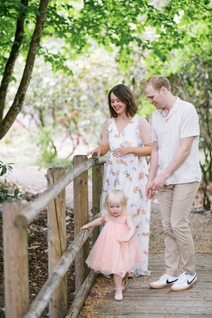 A family walks together on a wooden pathway through lush greenery on a bright spring day.