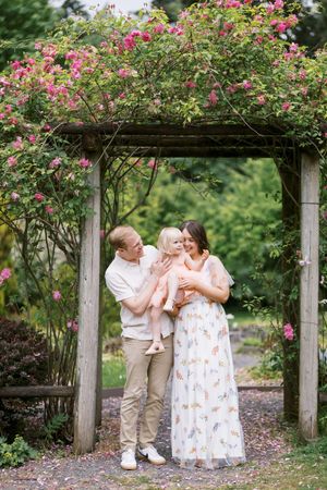 A romantic couple shares playful moments under a rose-covered garden pergola on a sunny summer day.