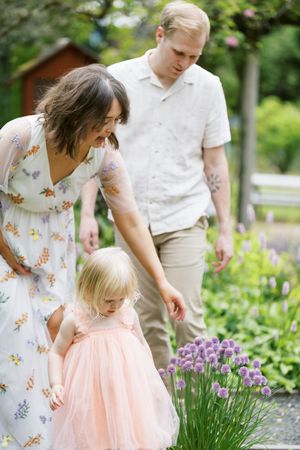 Family exploring summer garden with blooming allium and pink flowers along gravel path.