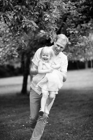 Black and white photo sequence of a parent playfully swinging a joyful toddler in an outdoor garden setting.