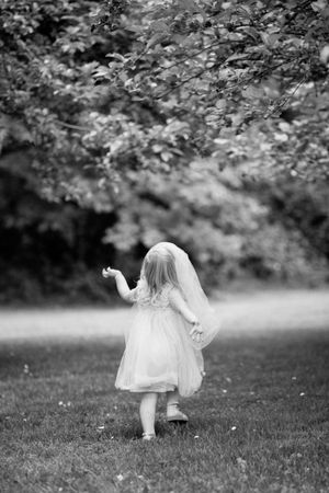 A playful black and white image sequence shows a figure in a flowing white dress twirling and dancing on grass outdoors.