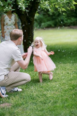 A heartwarming moment shared on a summer day in a garden with bubbles floating through the air and a pink dress twirling.