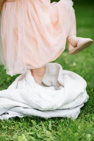 A close-up of flowy peach and white fabric from a dress trailing gracefully across green grass.