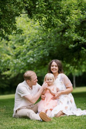 A gentle outdoor family portrait in a lush green park setting with everyone wearing light spring-colored outfits.