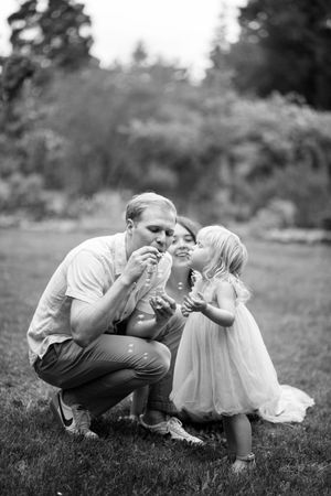A family blows bubbles together outdoors in a black and white photo captured in a garden setting.