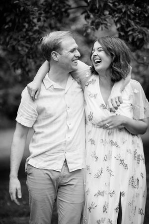 A joyful couple laughs together outdoors in black and white, wearing light summer clothing.