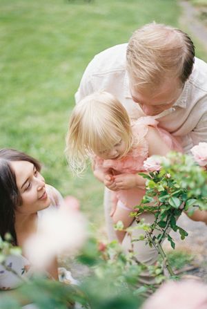 A family shares a tender moment together while exploring roses in a garden on a sunny day.