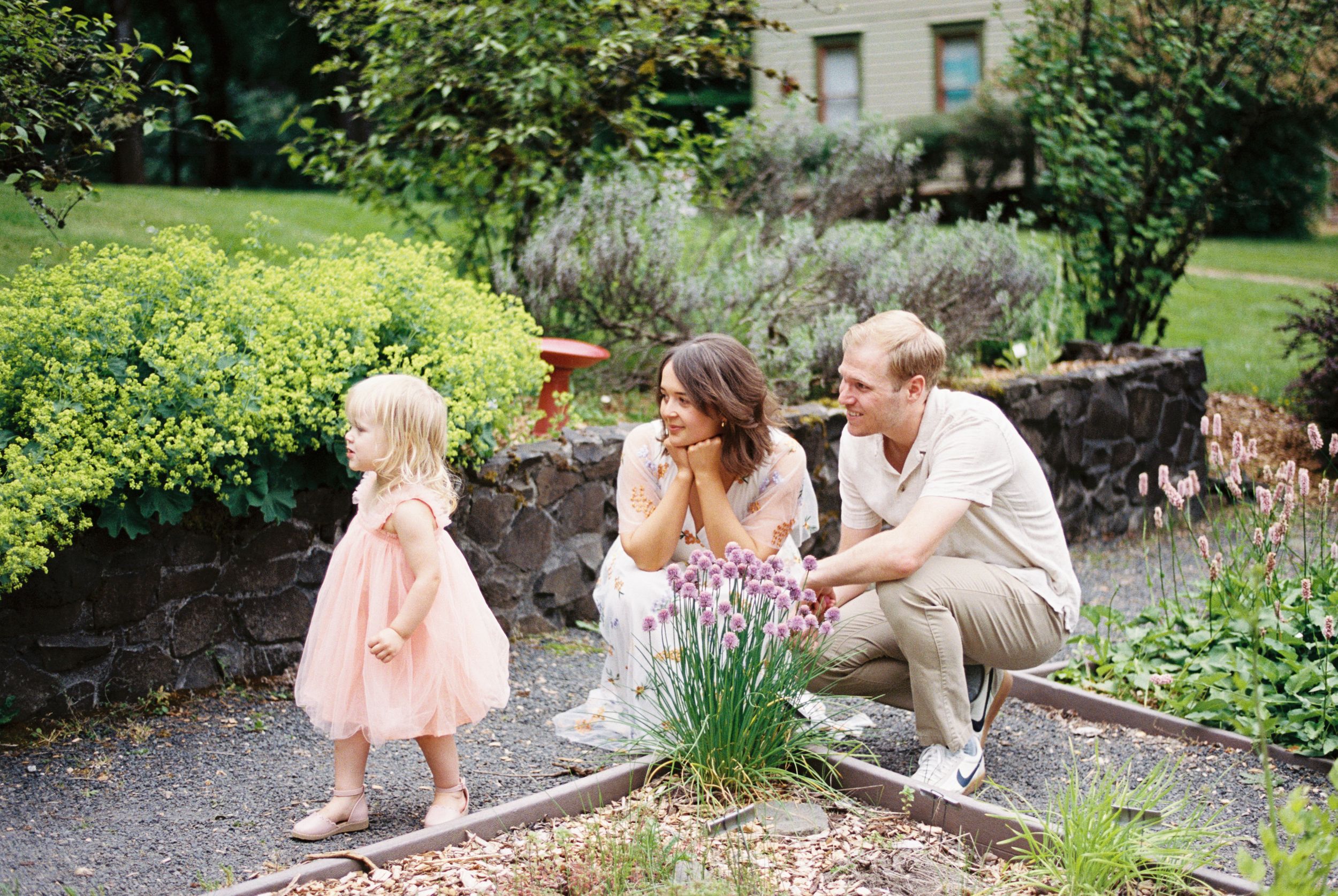 A family admires blooming lavender plants in a spring garden outside a stone house.