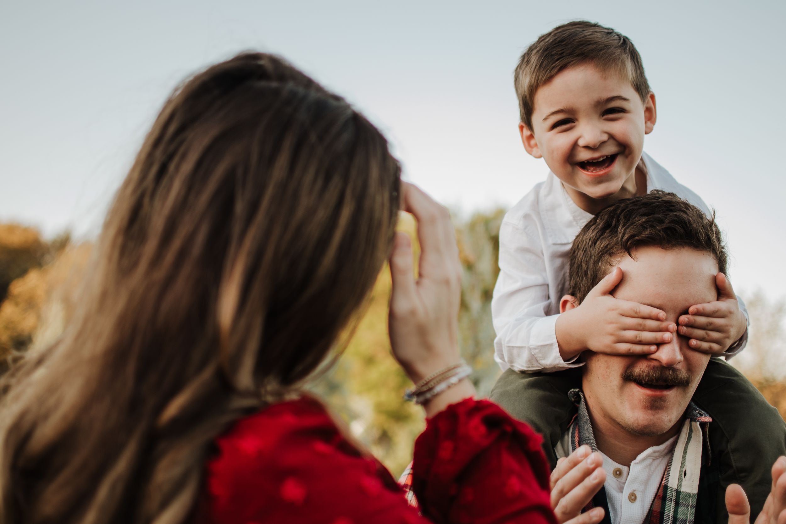 Playful family moment outdoors with child covering eyes and laughing.