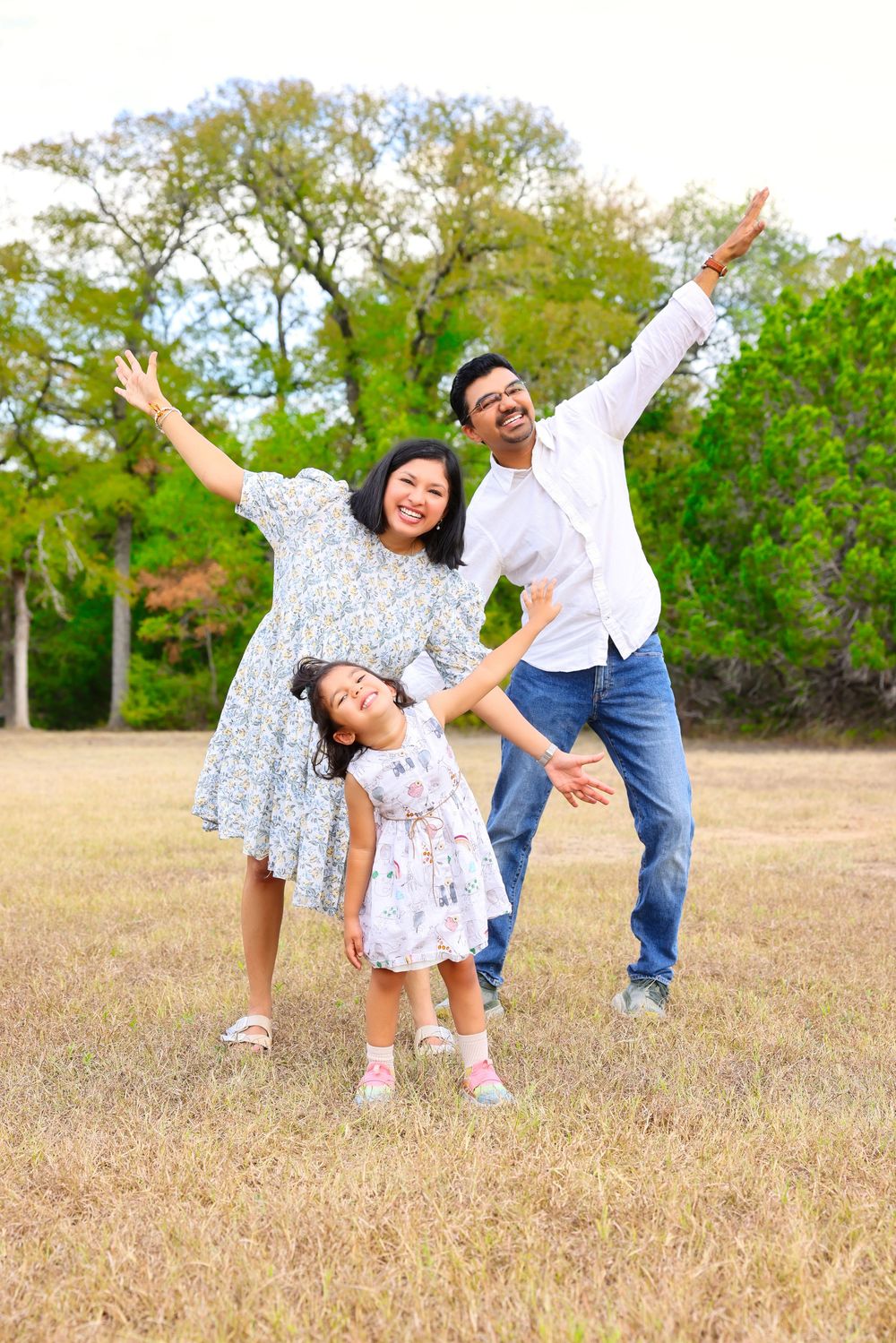 Family plays together outdoors in a field on a sunny day, striking playful poses in matching outfits.